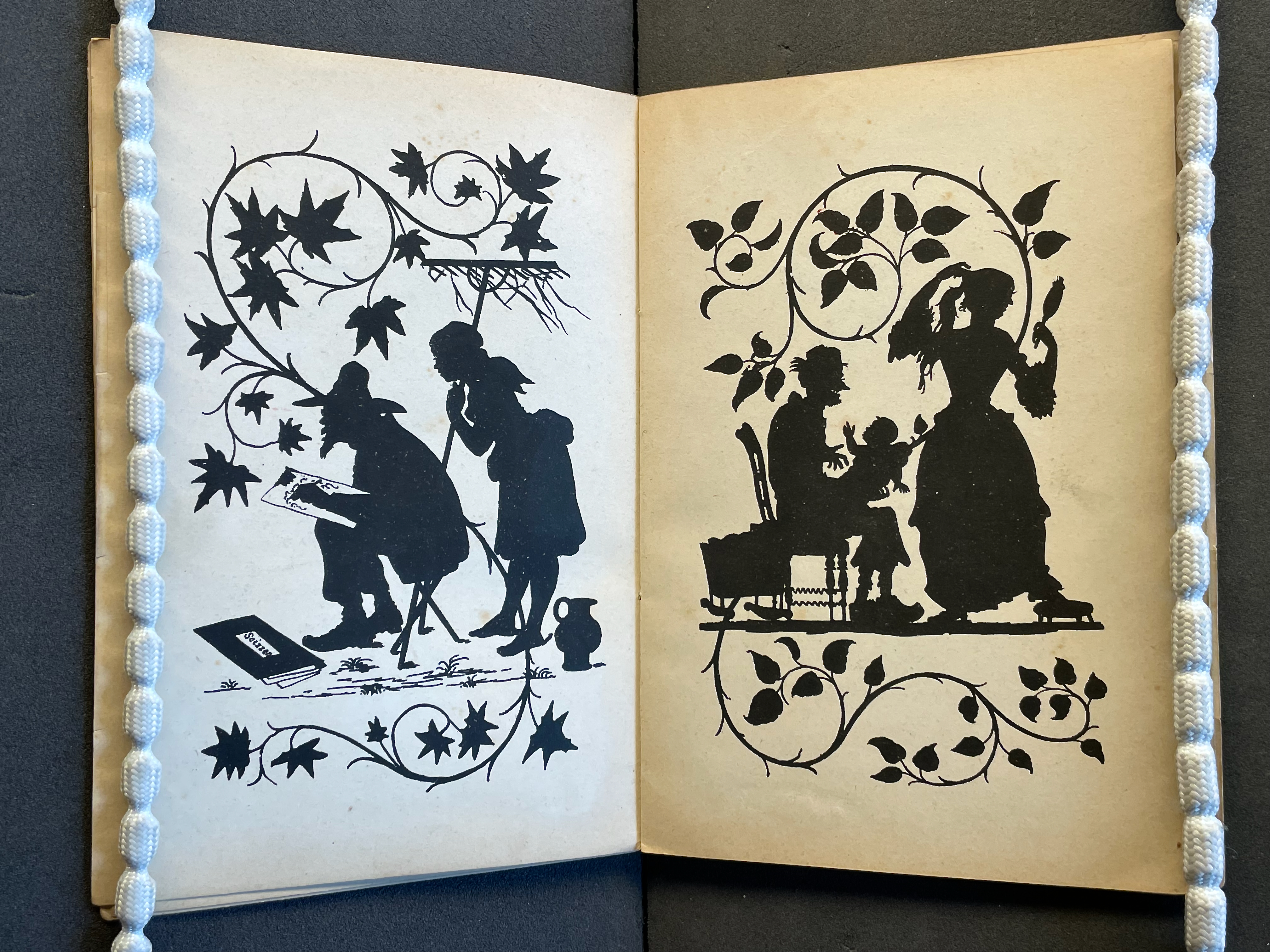 Silhouettes of two figures outdoors, one sketching while the other observes, framed by decorative leaves.