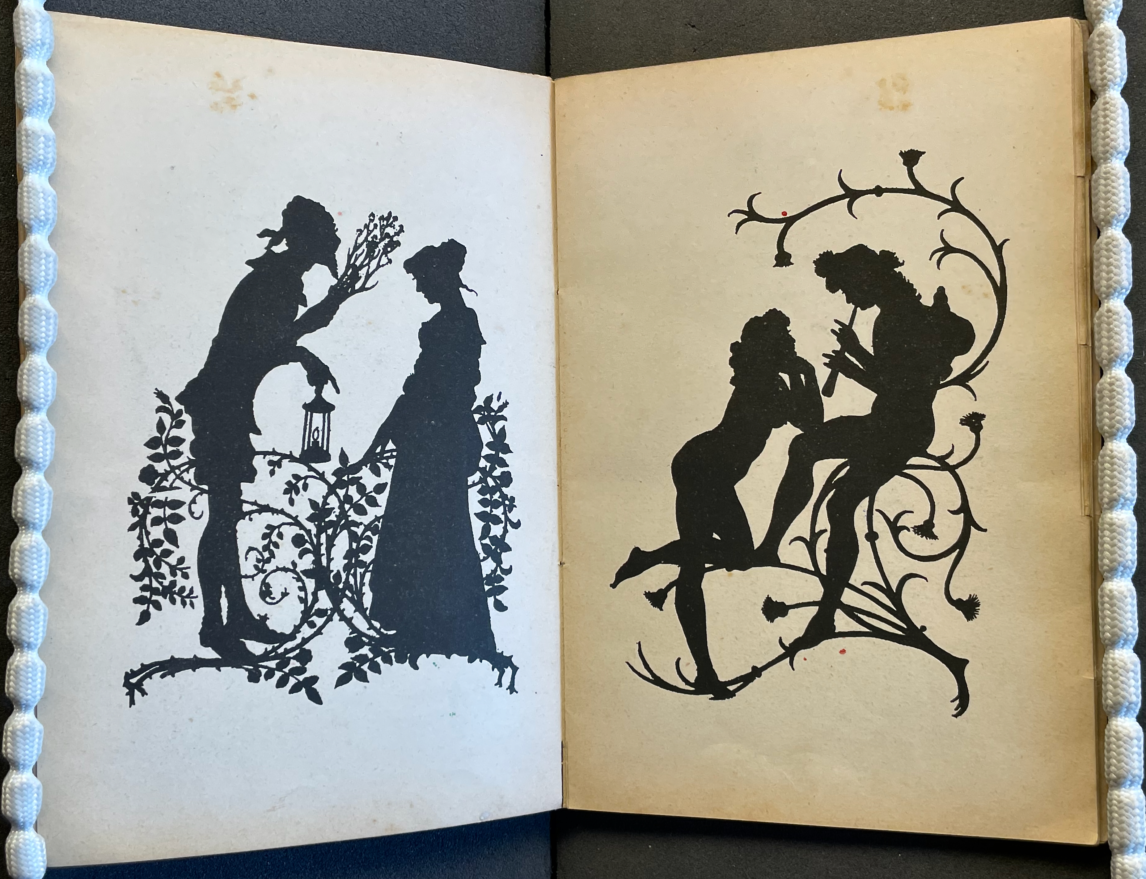 A vintage illustration showcasing two scenes in black silhouettes against a light background. On the left, a man presents flowers to a woman near decorative vines. On the right, a man plays a flute while a woman leans towards him, surrounded by floral designs.