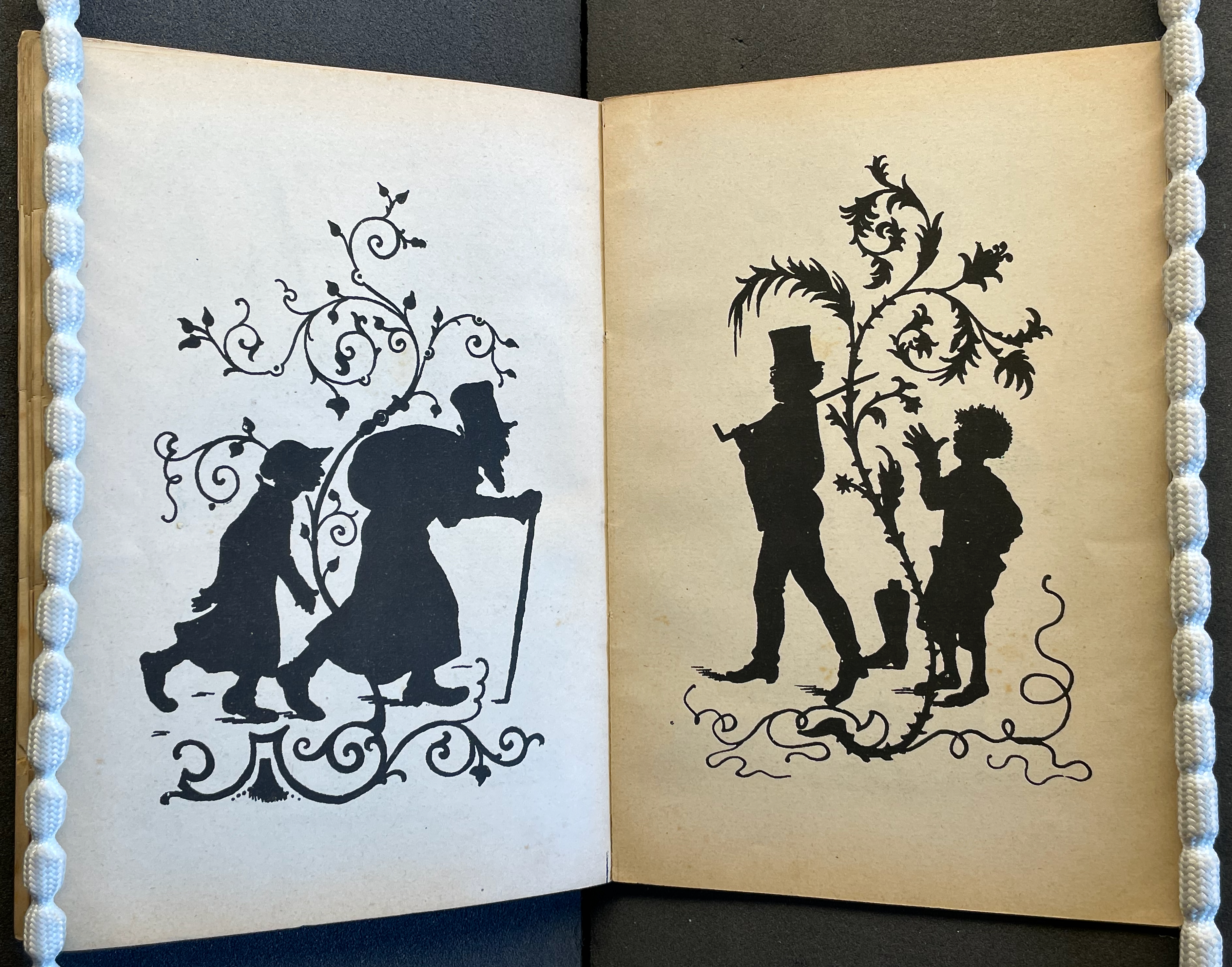 A vintage illustration featuring two black silhouettes: on the left, a child walking hand in hand with an elderly figure holding a cane, surrounded by decorative vines; on the right, a man in a top hat walking alongside a child, both against a backdrop of intricate foliage.
